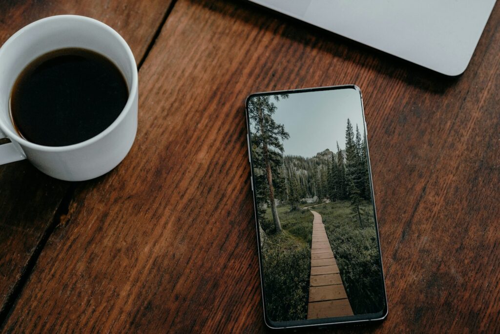 Celular sobre mesa de madeira ao lado de uma xícara de café, sugerindo uma pausa