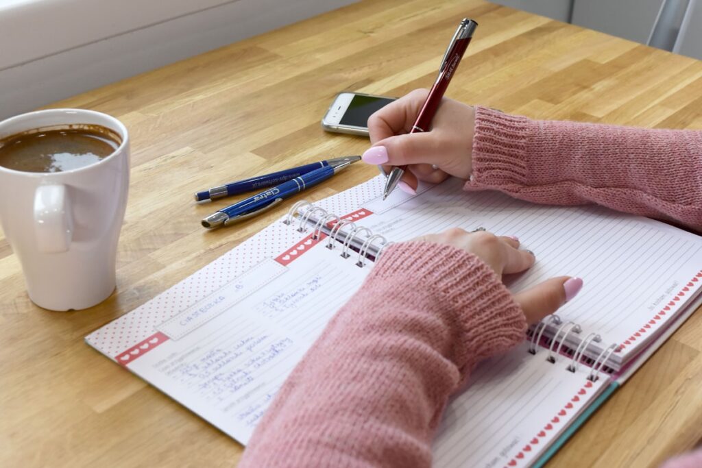 pessoa escrevendo em caderno de journaling com xícara de café ao lado