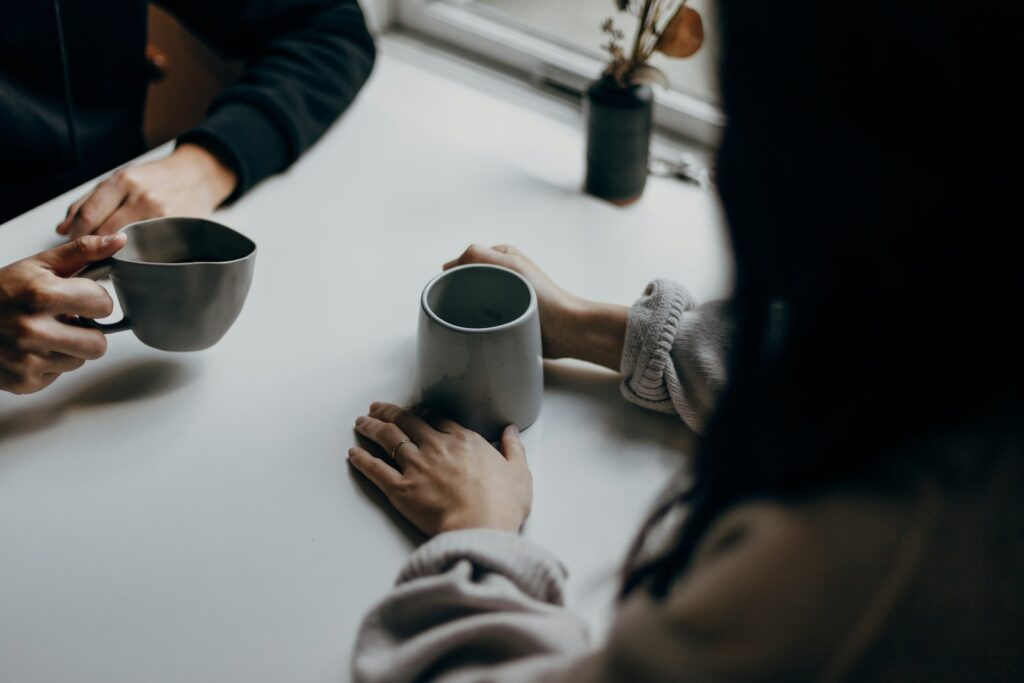 Duas pessoas conversando à mesa, cada uma segurando uma xícara