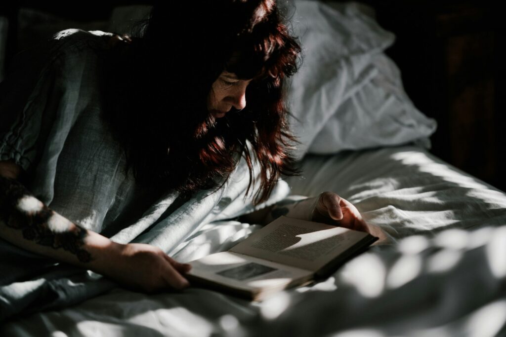Mulher deitada na cama à noite, iluminada por luz quente, lendo um livro antes de dormir