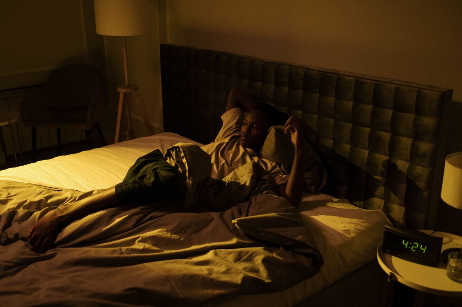 Acordar de madrugada: homem acordado na cama à noite com o relógio ao lado