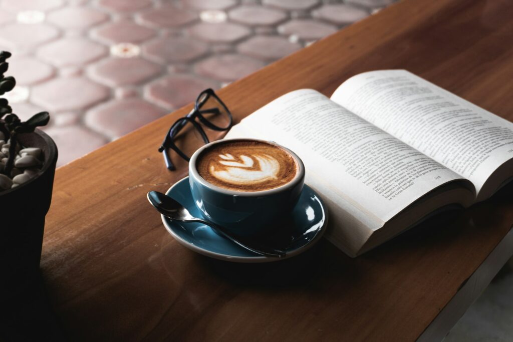 Livro aberto ao lado de uma xícara de café sobre uma mesa de madeira