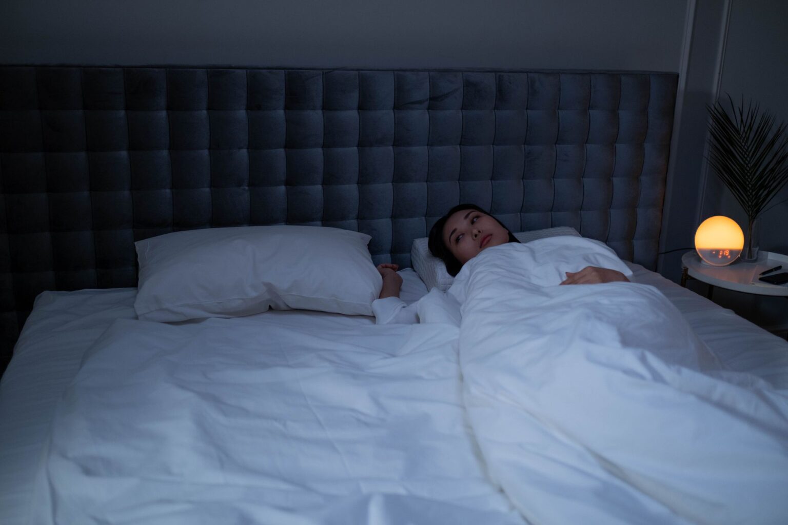 Insônia: mulher acordada na cama durante a noite, com luminária acesa