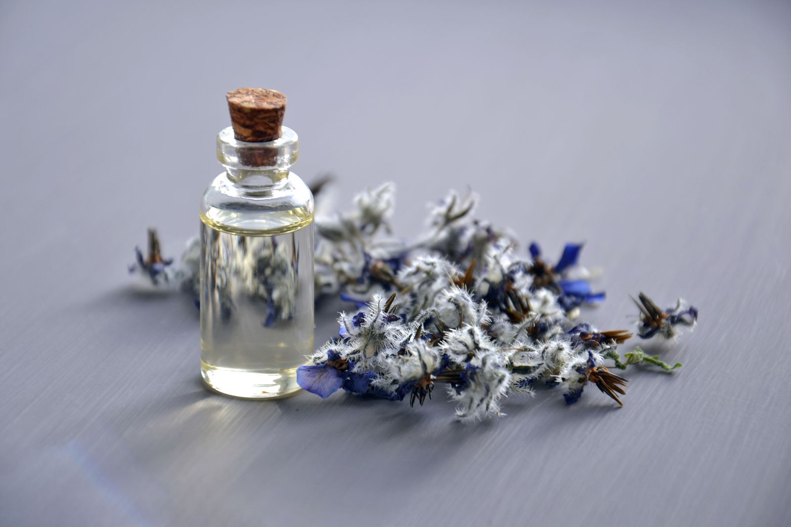 óleo essencial de lavanda: frasco de vidro ao lado de flores secas de lavanda