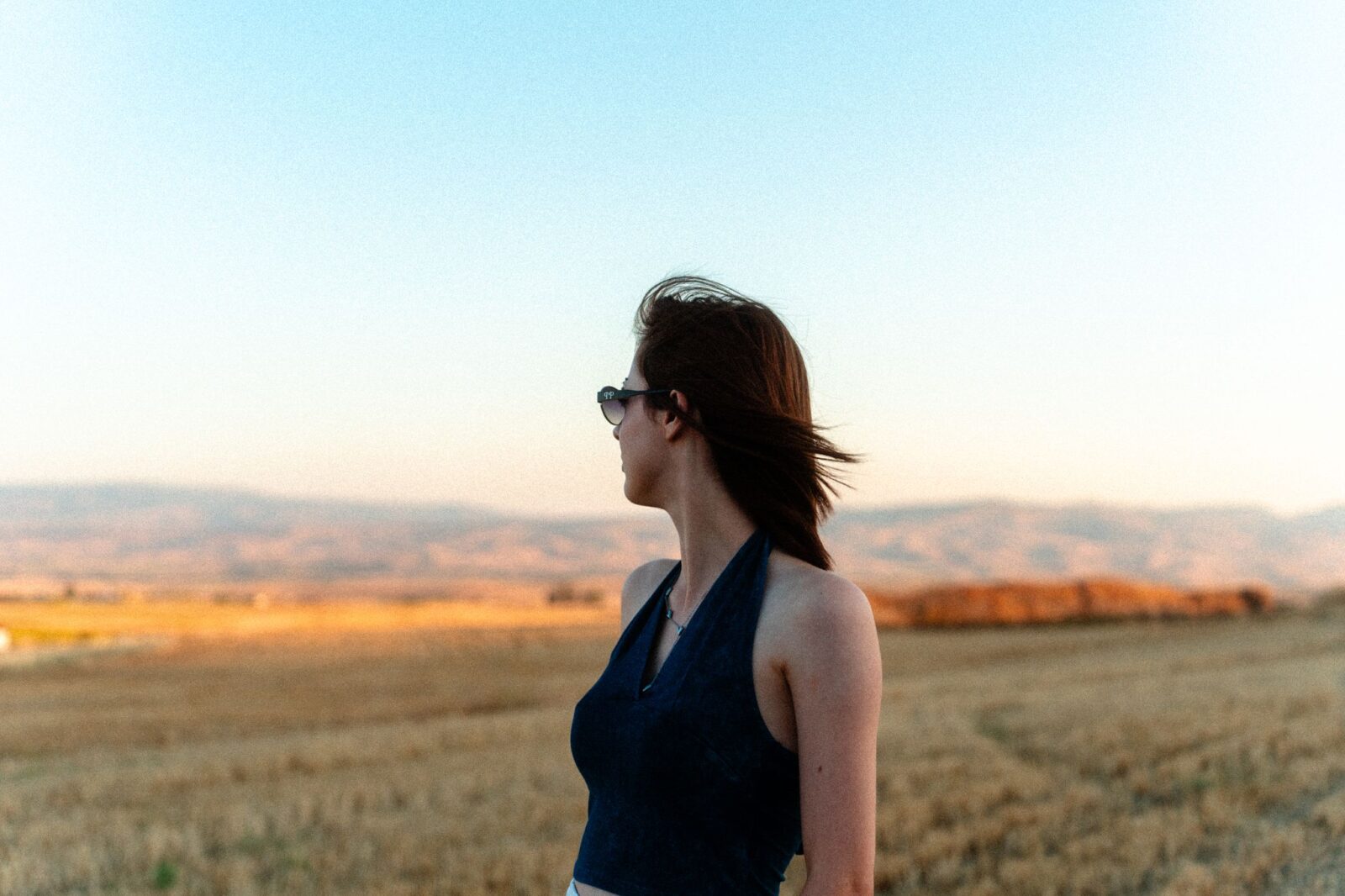 Relacionamento abusivo: mulher olhando o horizonte em um campo ao pôr do sol, em momento de reflexão