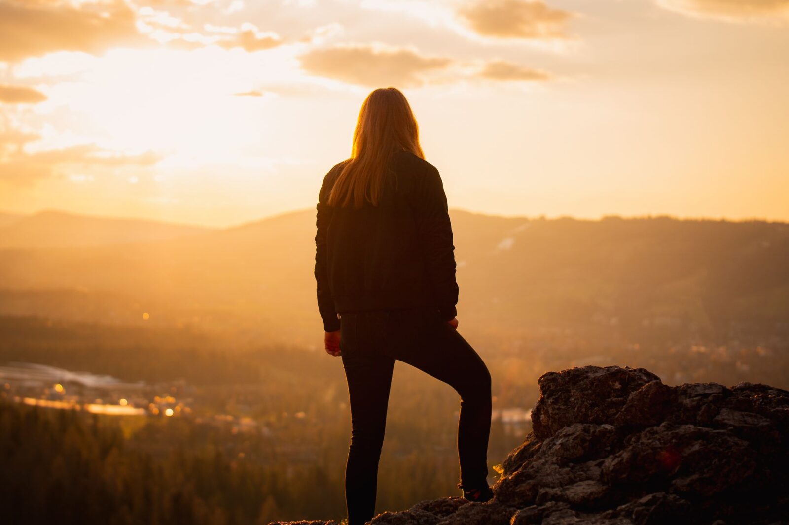 Resiliência: mulher de pé sobre uma rocha observando o nascer do sol nas montanhas
