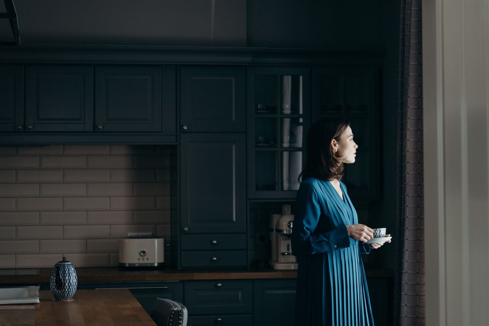 Mulher segurando uma xícara de chá na cozinha e olhando pela janela, fazendo uma pausa antes de comer