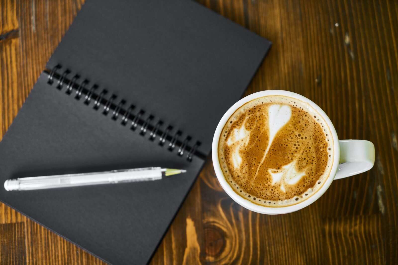 Caderno espiral aberto com caneta ao lado de uma xícara de café, para o diário de gratidão