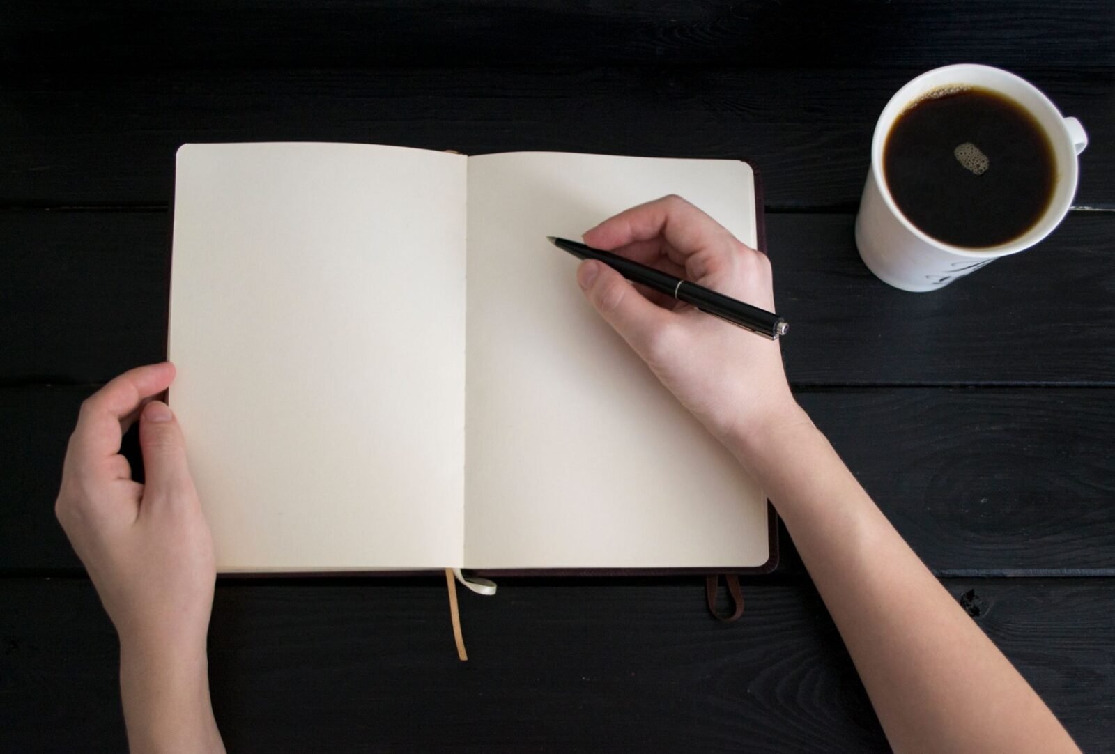 Diário de gratidão: mãos escrevendo num caderno aberto, com uma xícara de café ao lado