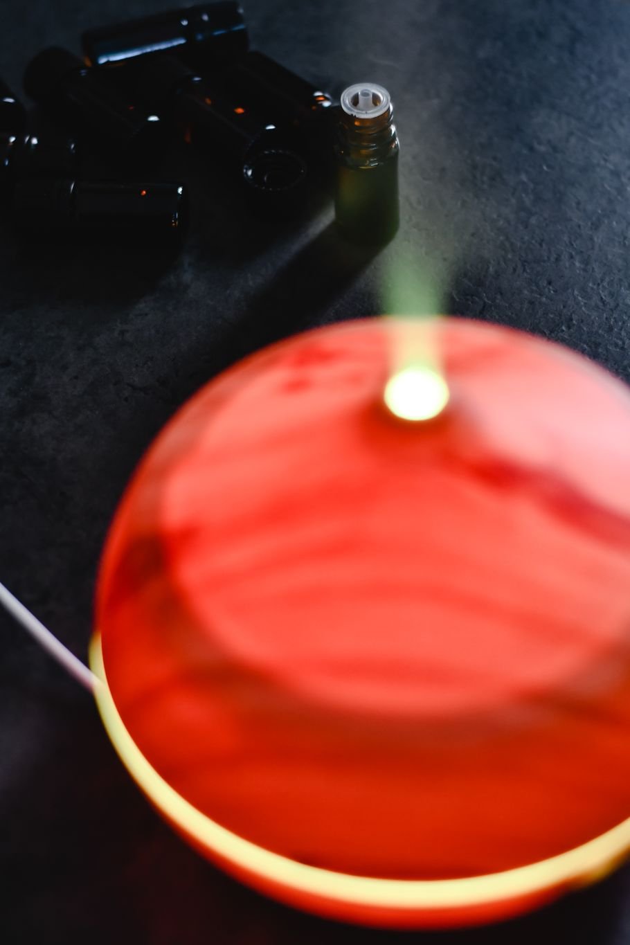 Difusor de aromas portátil iluminado liberando névoa, com frascos de óleo essencial ao fundo
