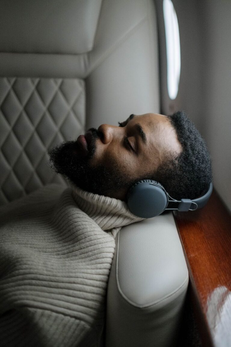 Homem dormindo sentado numa poltrona de avião, com fones de ouvido e a cabeça encostada no assento