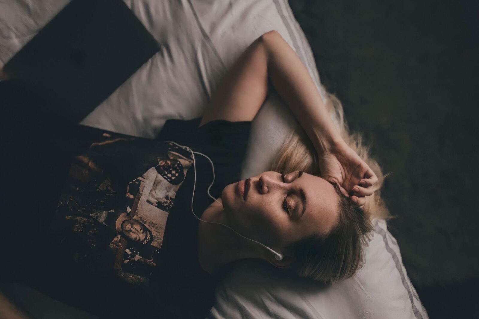 Fone de ouvido para dormir: mulher deitada na cama, de olhos fechados, ouvindo algo com fones de ouvido com fio