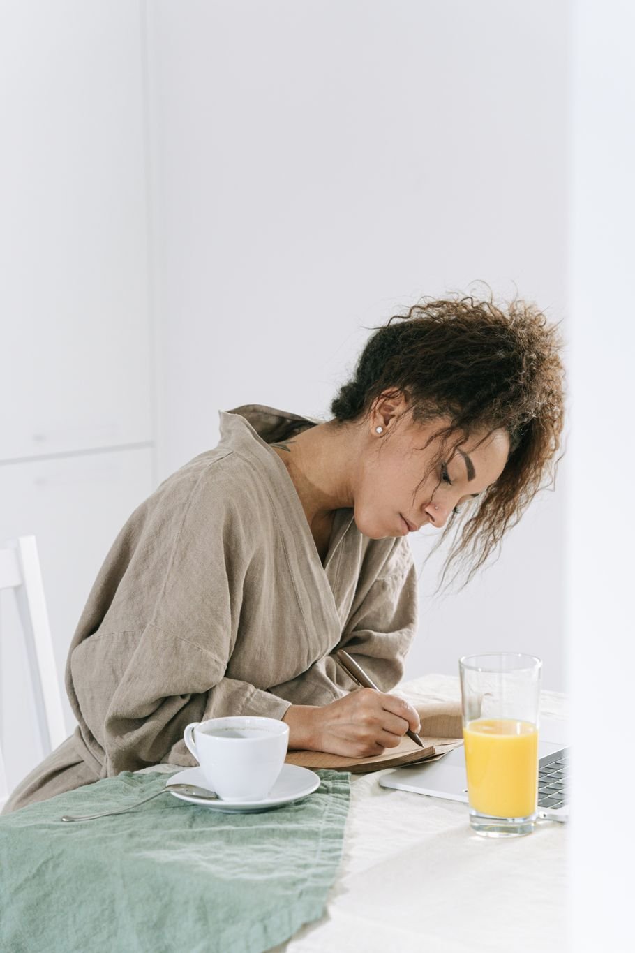 Escrita matinal: mulher de roupão escrevendo num caderno à mesa, com café e suco ao lado