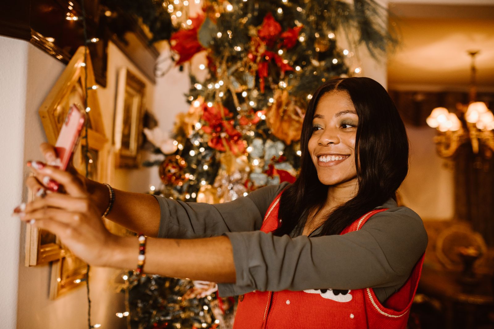 Mulher sorrindo enquanto tira uma selfie diante de uma árvore de Natal iluminada