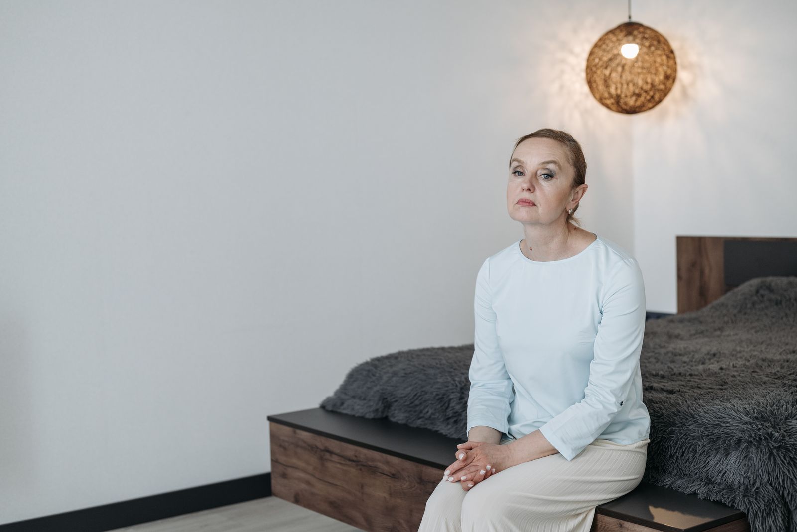 Mulher de meia-idade sentada na beira da cama, com expressão pensativa