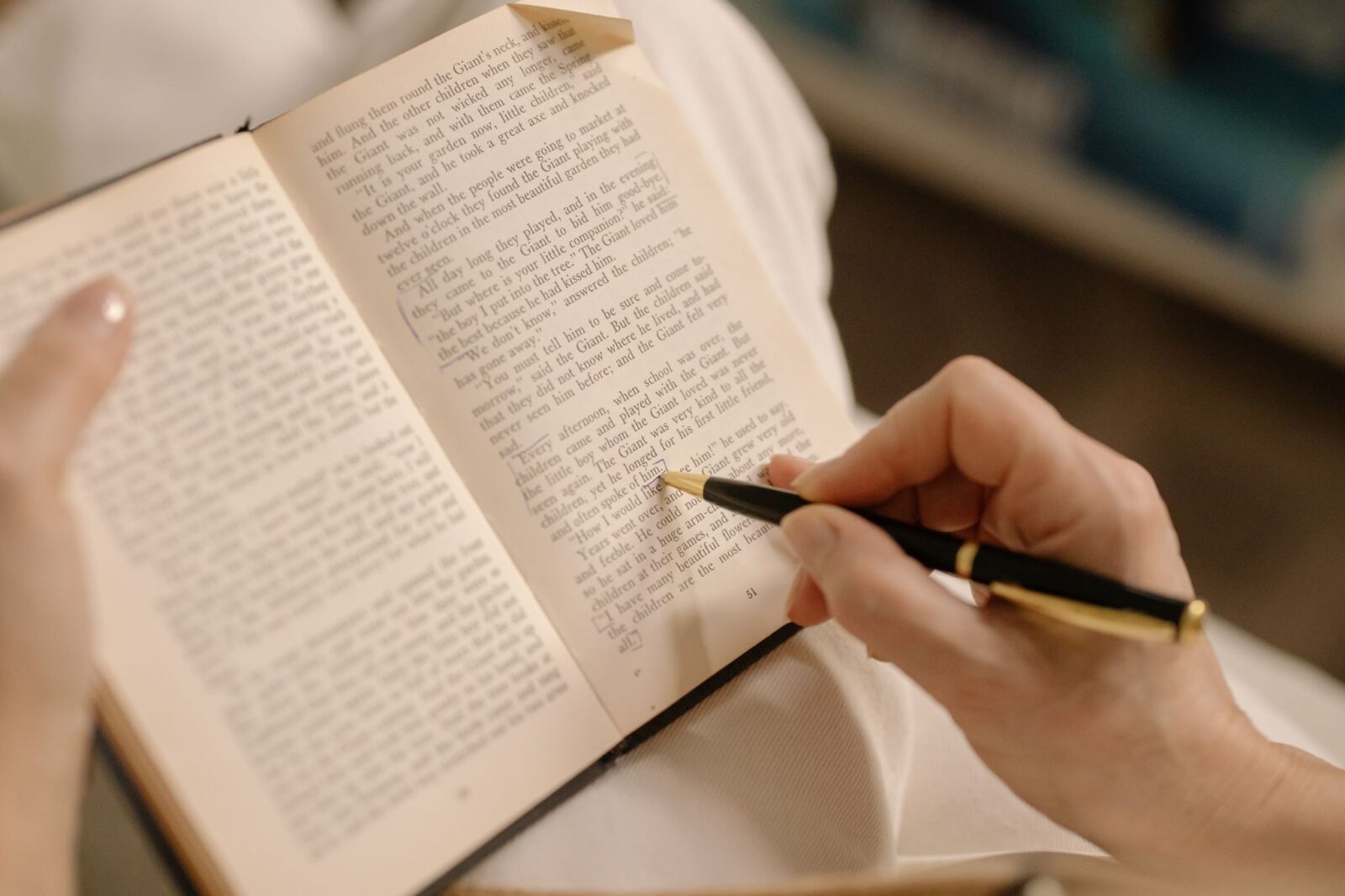 pessoa segurando um livro aberto e sublinhando um trecho com caneta