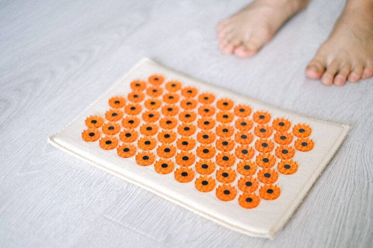 Tapete de acupressão com pontas plásticas laranja no chão, ao lado de pés descalços