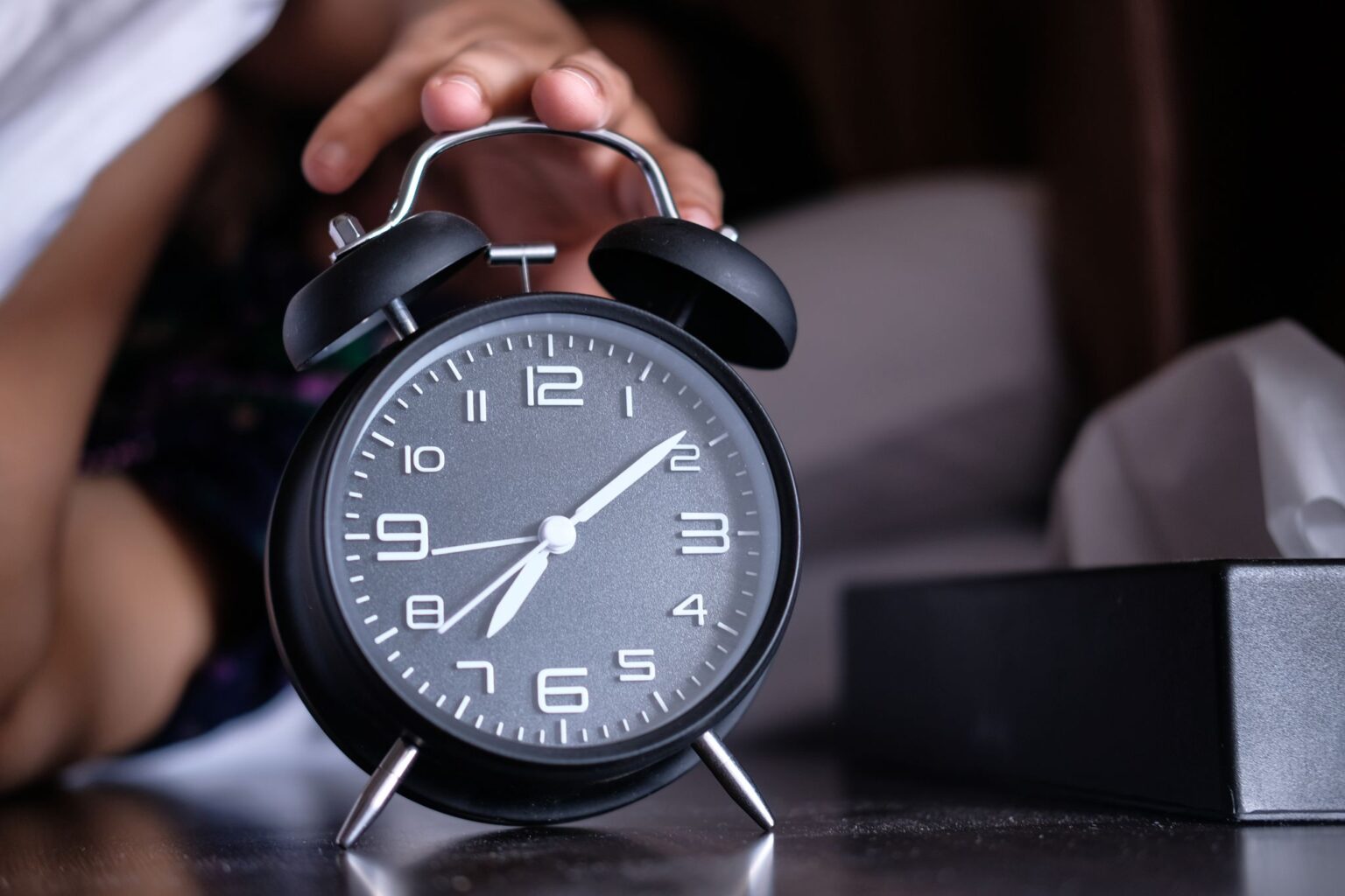 Despertador ao lado da cama, lembrando a importância do sono