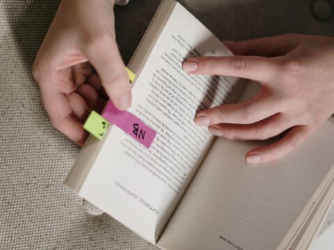 Mãos colando marcadores de página adesivos coloridos em um livro aberto