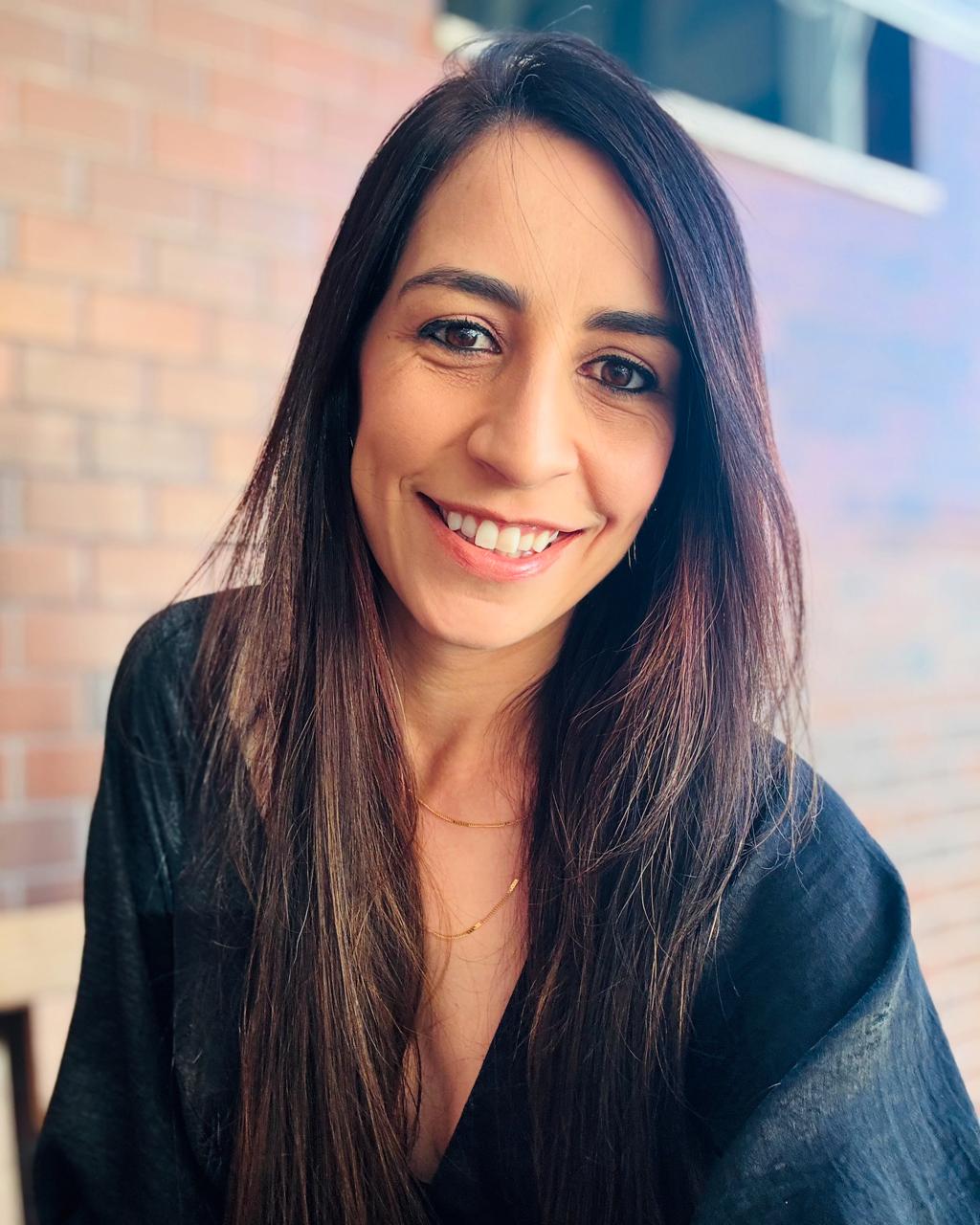 Retrato da psicóloga Lígia Daher, sorrindo, diante de uma parede de tijolos